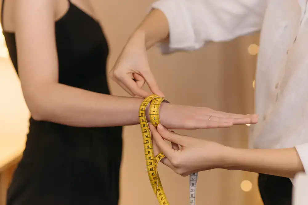 Milliner measuring a client's head with a soft yellow measuring tape